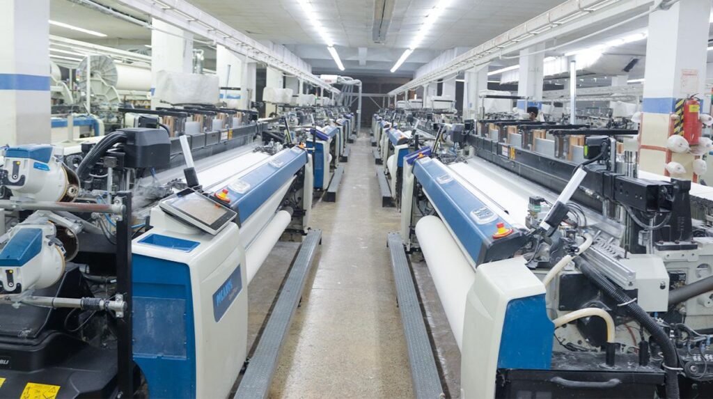 Worker operating a power loom at a textile weaving facility