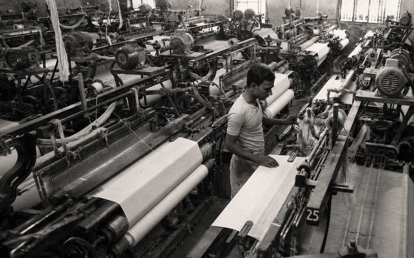 Worker operating a power loom at a textile weaving facility